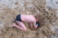 Child boy playing on sand beach digging shovel deep hole on summer vacation.