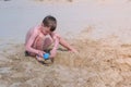 Child boy playing on sand beach digging shovel and trying to build sand tower.