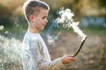 Child boy playing with smoking wooden stick outdoors