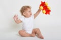 Child boy playing with toys indoors, sitting on floor and raising hands up, holding red and yellow toy car, looking at it with big Royalty Free Stock Photo