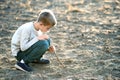 Child boy playing with wooden stick digging in black dirt ground outdoors Royalty Free Stock Photo