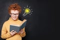 Child boy reading a book, having fun and idea lightbulb on blackboard background in classroom Royalty Free Stock Photo