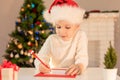 Child boy in red Santa hat writing a letter to Santa Claus. Christmas or New Year cozy holidays concept. Xmas time Royalty Free Stock Photo