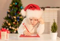 Child boy in red Santa hat writing a letter to Santa Claus. Christmas or New Year cozy holidays concept. Xmas time Royalty Free Stock Photo