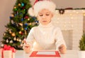 Child boy in red Santa hat writing a letter to Santa Claus. Christmas or New Year cozy holidays concept. Xmas time Royalty Free Stock Photo