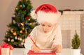 Child boy in red Santa hat writing a letter to Santa Claus. Christmas or New Year cozy holidays concept. Xmas time Royalty Free Stock Photo