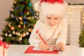 Child boy in red Santa hat writing a letter to Santa Claus. Christmas or New Year cozy holidays concept. Xmas time Royalty Free Stock Photo