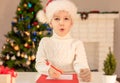 Child boy in red Santa hat writing a letter to Santa Claus. Christmas or New Year cozy holidays concept. Xmas time Royalty Free Stock Photo