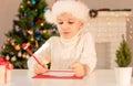 Child boy in red Santa hat writing a letter to Santa Claus. Christmas or New Year cozy holidays concept. Xmas time Royalty Free Stock Photo