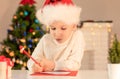 Child boy in red Santa hat writing a letter to Santa Claus. Christmas or New Year cozy holidays concept. Xmas time Royalty Free Stock Photo