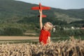 Child boy in red T-shirt plays with toy plane in wheat field on mountains background. Concept of flights and travel with children Royalty Free Stock Photo