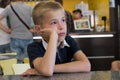 Child boy sitting in fast food restaurant behind empty table waiting for food Royalty Free Stock Photo