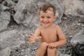 The child boy is sitting, smiling and sunbathing on large boulders, on the beach near the sea. Royalty Free Stock Photo