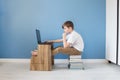 Child boy sitting on stack of books typing on his laptop, studying online at home, modern interior with blue wall background Royalty Free Stock Photo