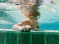 A child boy is swimming underwater in a pool, smiling and holding breath, with swimming glasses Royalty Free Stock Photo