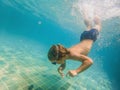 A child boy is swimming underwater in a pool, smiling and holding breath, with swimming glasses Royalty Free Stock Photo