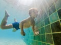 A child boy is swimming underwater in a pool, smiling and holding breath, with swimming glasses Royalty Free Stock Photo