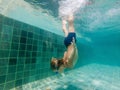 A child boy is swimming underwater in a pool, smiling and holding breath, with swimming glasses Royalty Free Stock Photo