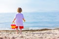 Child boy with a toy bucket in his hands standing on the sea beach, rear view with copy space Royalty Free Stock Photo