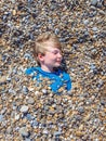 Child boy under pebbles stones on british seaside beach on sunny day