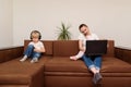 Child boy uses phone while mom works with laptop. Single mother concept