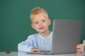 Child boy using a laptop computer at school. Cute pupil face closeup on blackboard background. Royalty Free Stock Photo