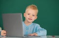 Child boy using a laptop computer at school. Cute pupil face closeup on blackboard background. Royalty Free Stock Photo