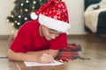 Child boy wearing Santa hat writing Christmas letter to Santa Claus at home near the Christmas tree Royalty Free Stock Photo