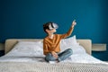 Child boy wearing virtual reality headset sitting on bed at home exploring metaverse. VR concept