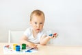 Child boy 2 years old sitting at a table on a white isolated background and paints, early development, place for text Royalty Free Stock Photo