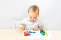 Child boy 2 years old sitting at a table on a white isolated background and paints, early development, place for text Royalty Free Stock Photo