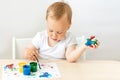 Child boy 2 years old sitting at a table on a white isolated background and paints, early development, place for text Royalty Free Stock Photo