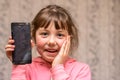 The child broke the telephone communicator and laughs. Baby joked breaking smartphone screen. Portrait of a cheerful little girl