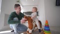 Child care, loving papa playing with merry toddler boy on plush steed seating and swinging at home in kitchen