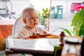 The child carefully looks ahead. Infant girl is sitting on a baby`s high chair in a street cafe.  Children  reading chooses and Royalty Free Stock Photo