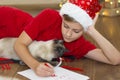 Child with a cat writing Christmas letter to Santa Claus. Boy wearing a Santa hat at home near the Christmas tree Royalty Free Stock Photo