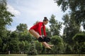 A child cheerleader in a red suit is exercising in the woods in nature with big pom-poms. Sports training for cheerleading.