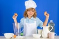 Child chef cook hold eggs prepares food in  blue studio background. Kids cooking. Teen boy with apron and chef Royalty Free Stock Photo