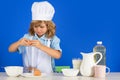 Child chef cook prepares food in isolated blue studio background. Kids cooking. Teen boy with apron and chef hat Royalty Free Stock Photo