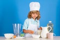 Child chef cook prepares food in isolated blue studio background. Kids cooking. Teen boy with apron and chef hat Royalty Free Stock Photo