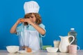Child chef cook prepares food in isolated blue studio background. Kids cooking. Teen boy with apron and chef hat Royalty Free Stock Photo