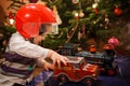 Child with Christmas present. Little boy playing with a toy car and red helmet under Christmas tree. Decorated home for Royalty Free Stock Photo