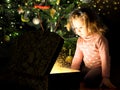 Child by Christmas tree opens magic chest. Portrait of little girl looking inside of gift box at home Royalty Free Stock Photo