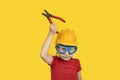 Child in construction helmet and goggles with holding pliers. Portrait on yellow background Royalty Free Stock Photo