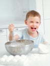 Child cooks food. Caucasian boy sits at table in kitchen and kneads dough in cup with hand whisk. Cheerful and positive Royalty Free Stock Photo