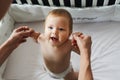 The child is in the crib. Portrait of a nine-month-old smiling baby girl standing in the playpen. Cheerful happy child