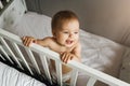 The child is in the crib. Portrait of a nine-month-old smiling baby girl standing in the playpen. Cheerful happy child Royalty Free Stock Photo