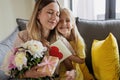 Child daughter congratulates mother and gives present card, gift and bouquet of flowers at home. Mom and girl smiling Royalty Free Stock Photo