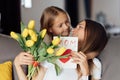 Child daughter congratulates mother and gives present card, gift and bouquet of flowers at home. Mom and girl smiling Royalty Free Stock Photo