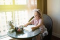 Child daughter painting postcard for mom. Girl sitting at home on table, next lying pink flower for mother. Mother day concept Royalty Free Stock Photo